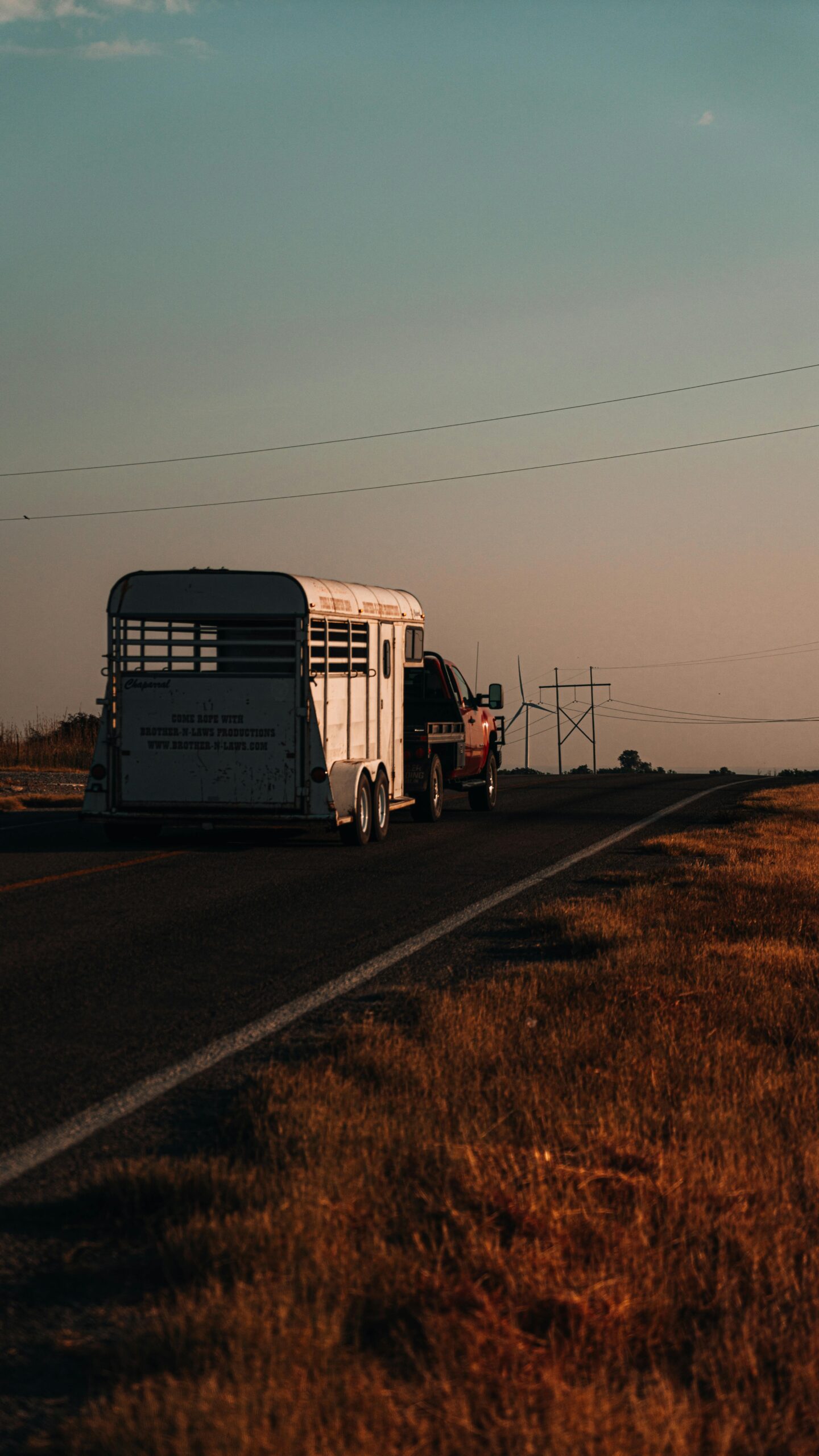 A truck towing a horse trailer down a rural road during sunset, depicting serene travel.